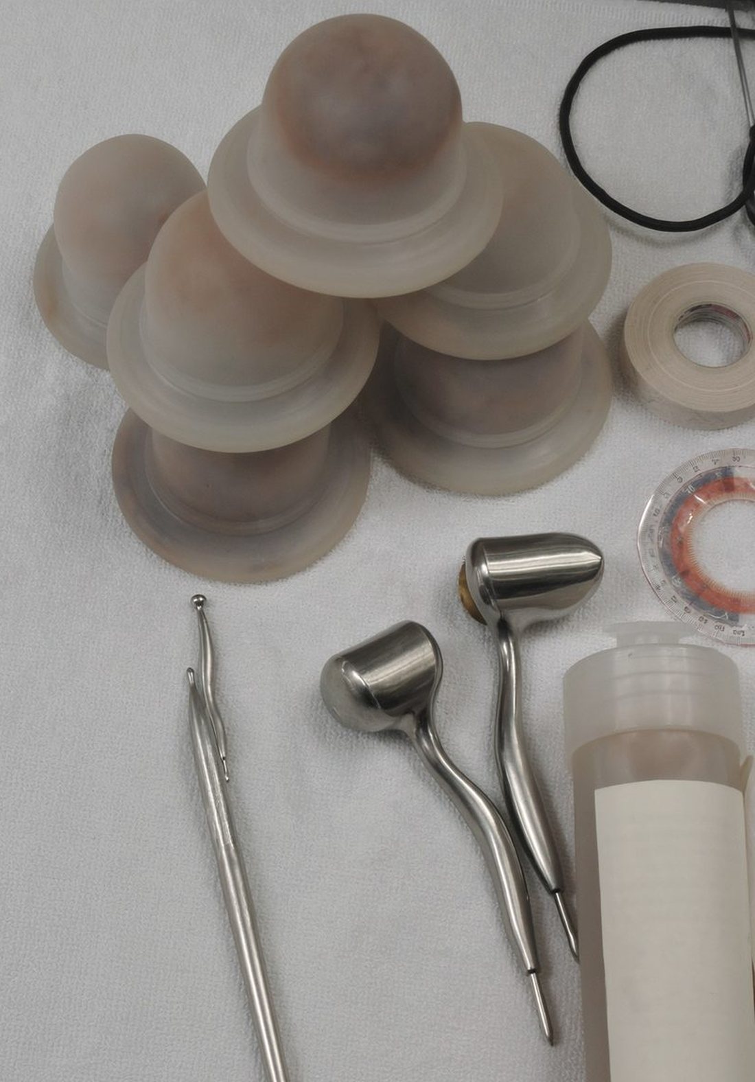 Laid out on a white towel: a stack of silicone cupping cups, two stainless steel soft tissue tools, a goniometer, a roll of tape and an unlabelled bottle of lotion.